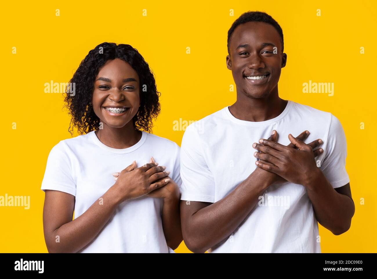 Donna africana e uomo che tengono entrambi i palmi sul petto Foto Stock