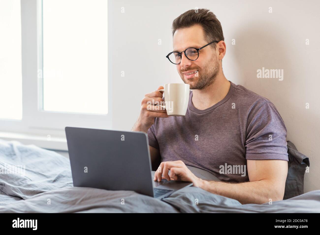 Uomo seduto con computer portatile in camera da letto guardando film on-line Foto Stock