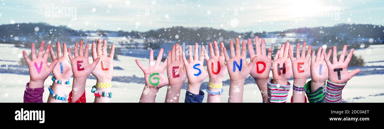 Le mani dei bambini che tiene la parola tedesca colorata Viel Gesundheit significa rimanere in buona salute. Neve Inverno sfondo con fiocchi di neve Foto Stock
