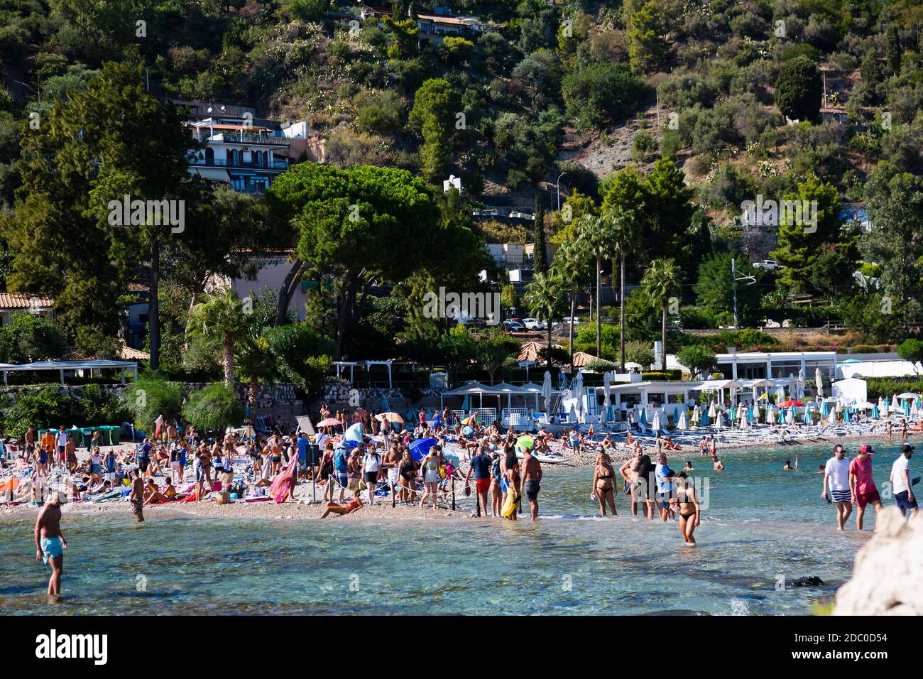 Sicilia, Italia. I turisti si sfilano attraverso acque poco profonde per raggiungere l'attrazione turistica Isola Bella vicino alla città siciliana di Taormina. Foto Stock