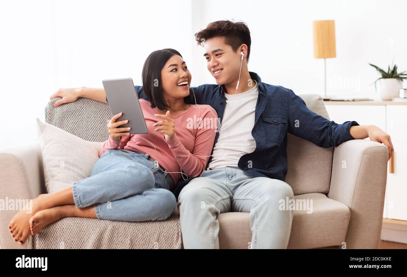 I coniugi giapponesi che usano il Internet di esplorazione della tavoletta seduti sul divano interno Foto Stock