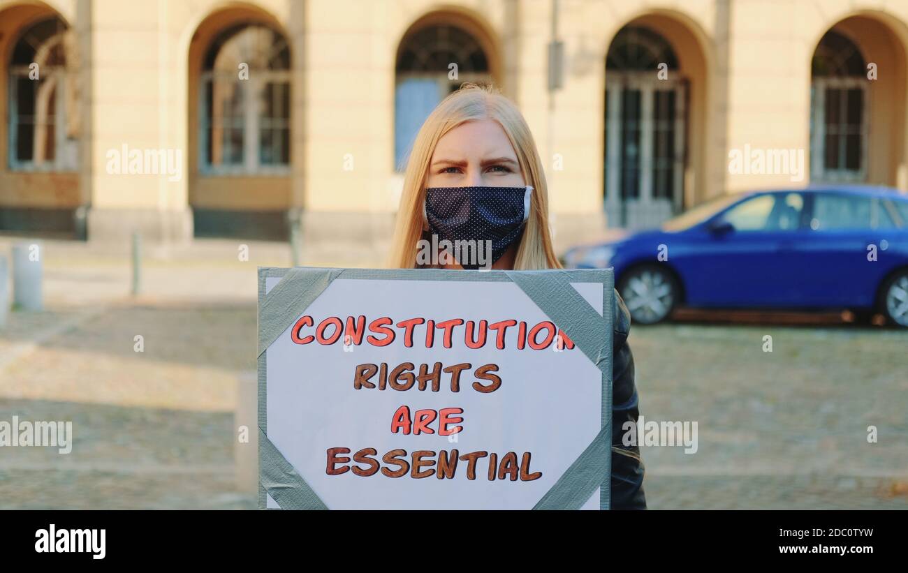 Protesta a piedi: Donna in maschera protettiva che sostiene per la protezione dei diritti costituzionali. Tiene la bandiera e va sulla strada. Foto Stock