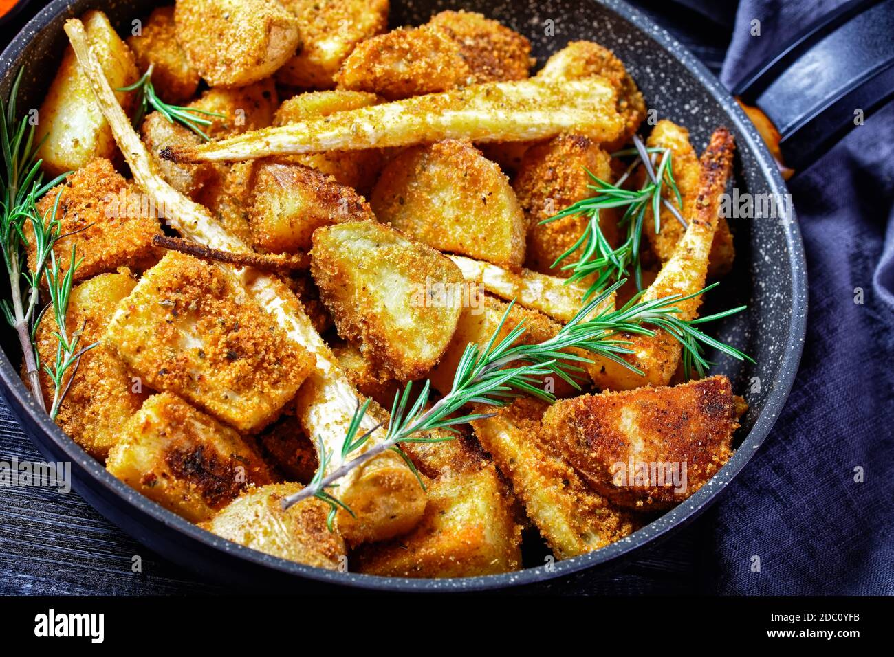 Verdure di radice al forno: Spicchi di patata e di pastinaca impanati con paprika affumicata e rametti di rosmarino fresco serviti su un backgrou di legno Foto Stock