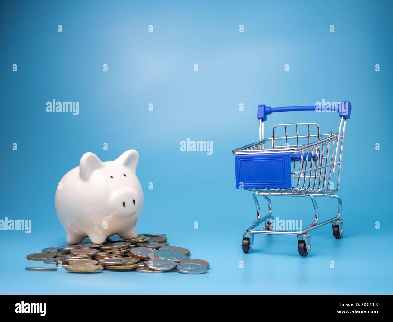 Un carrello con un mucchio di monete e una banca di Piggy su uno sfondo blu. Concetto di ipoteca. Soldi e casa. Stato finanziario. Foto Stock