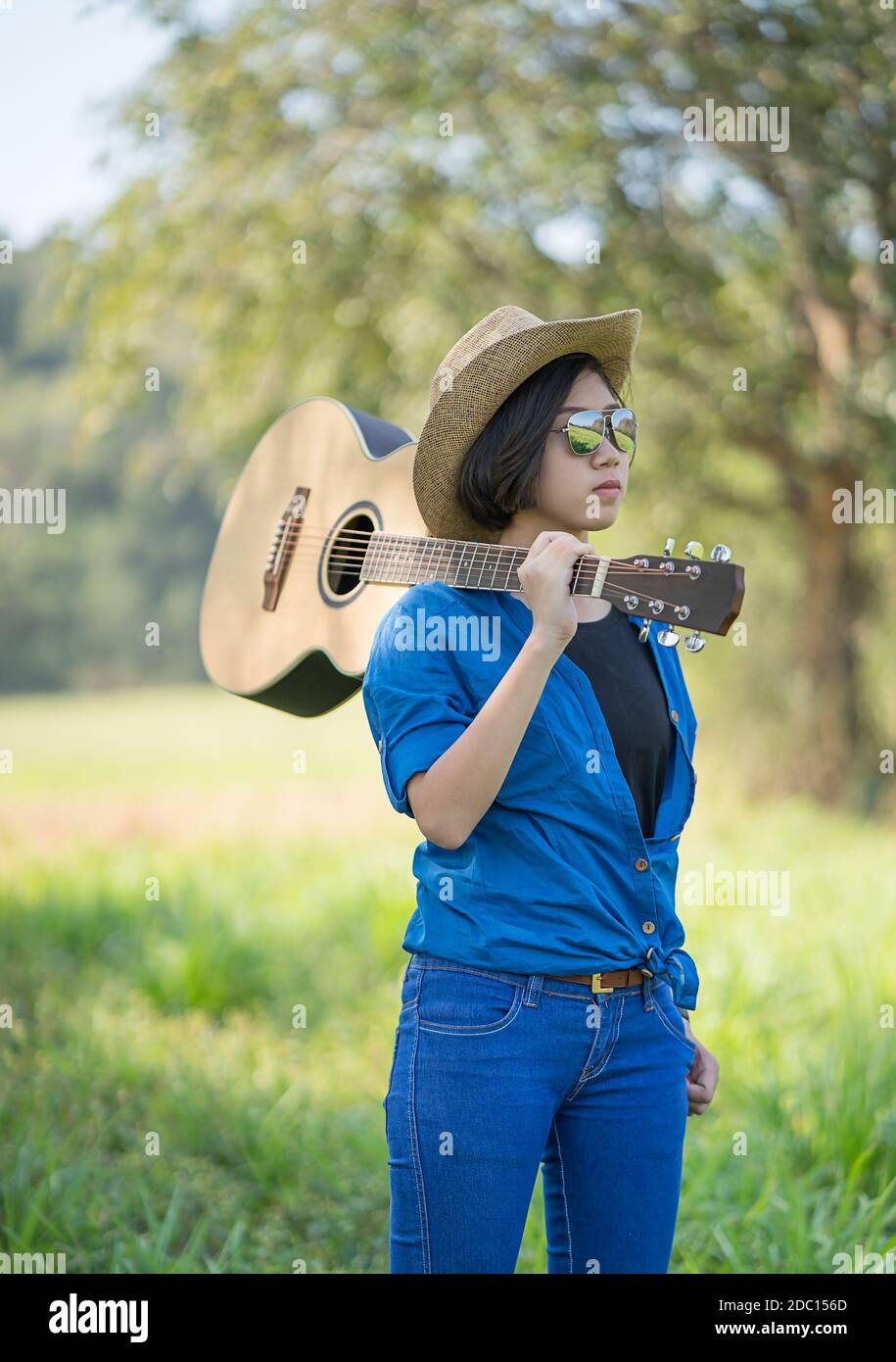 Giovane donna asiatica di capelli corti indossare un cappello e portare la  sua chitarra in erba campagna sul campo della Thailandia Foto stock - Alamy