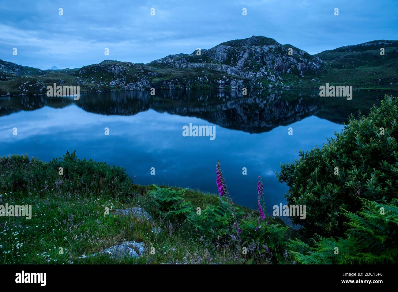 Una vista delle colline riflesse nelle acque ancora del Loch Gobloch al tramonto, vicino a Tarbet sulla costa nord occidentale della Scozia. Giugno. Foto Stock