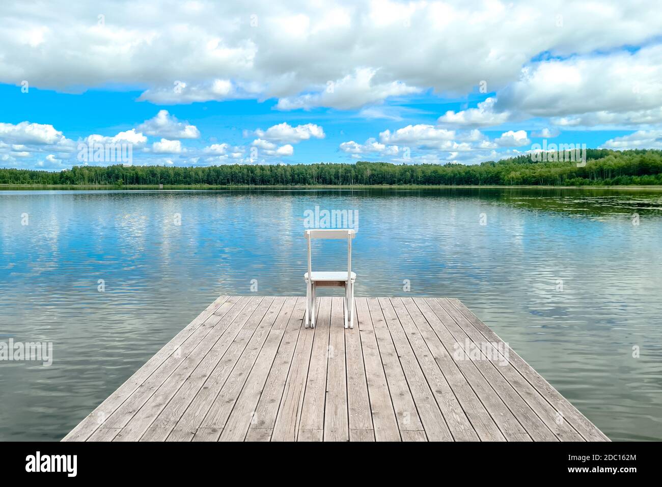 Sedia vuota in legno bianco presso il molo del lago di fronte a una splendida vista. Foto Stock