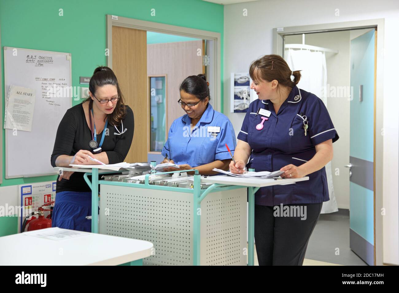 Moderno reparto ospedaliero del Regno Unito - stazione infermieri. Due infermieri discutono i documenti dei pazienti con una dottoressa. Foto Stock