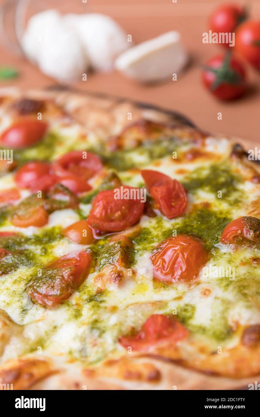 Pizza italiana con pomodori ciliegini, basilico al pesto e mozzarella cotta in forno a legna. Cucina italiana. Foto Stock