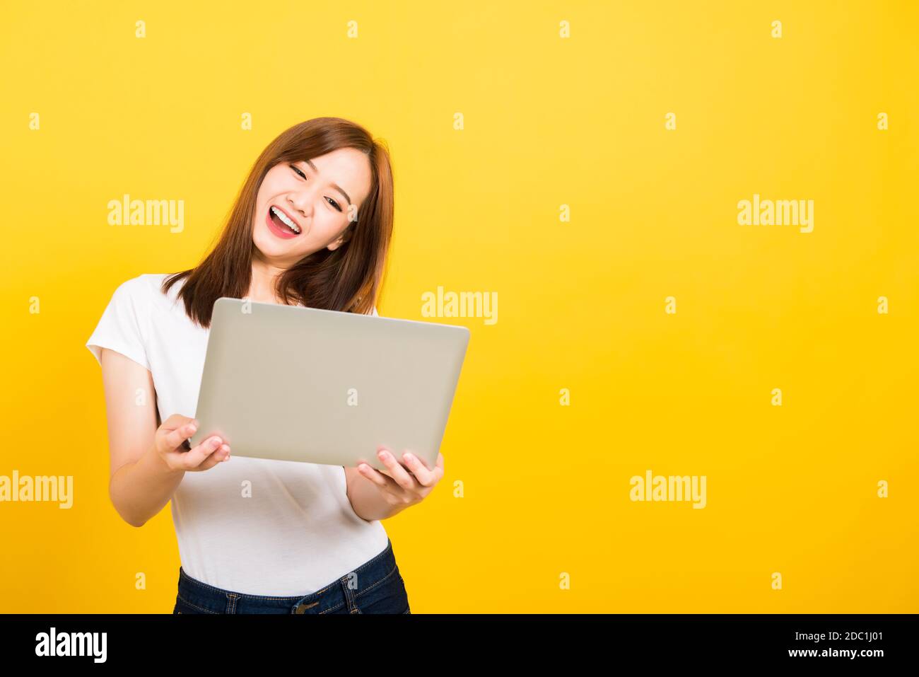 Asian Happy Portrait bella cute giovane donna teen sorriso in piedi indossare t-shirt tenere computer portatile ed eccitato celebrare il successo cercando di camer Foto Stock