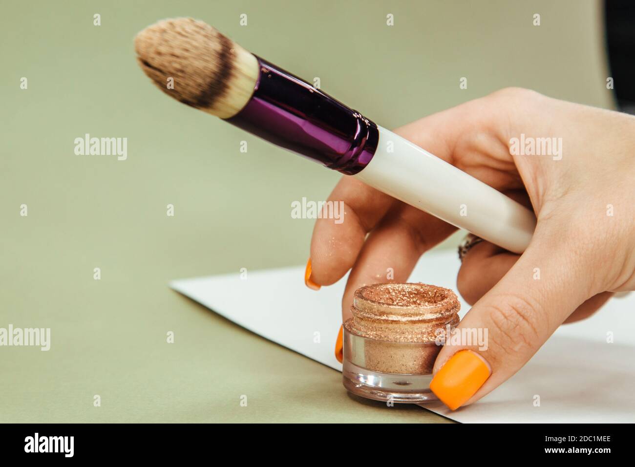 Scintille d'oro per il trucco in un vaso con una spazzola per applicarle su uno sfondo verde e bianco solido isolato. Foto Stock