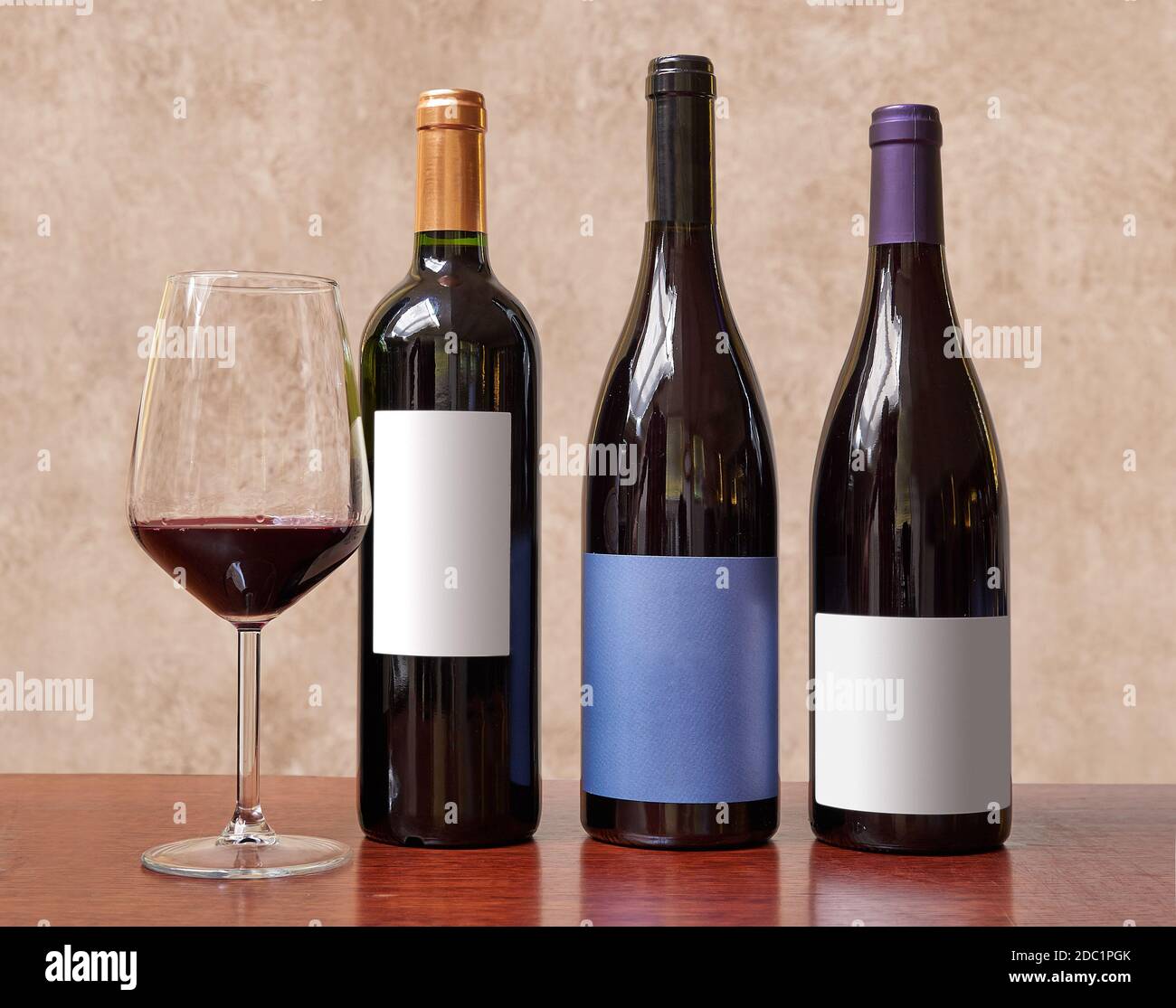 Tre bottiglie di vino e un bicchiere di vino rosso contro sfondo testurizzato Foto Stock