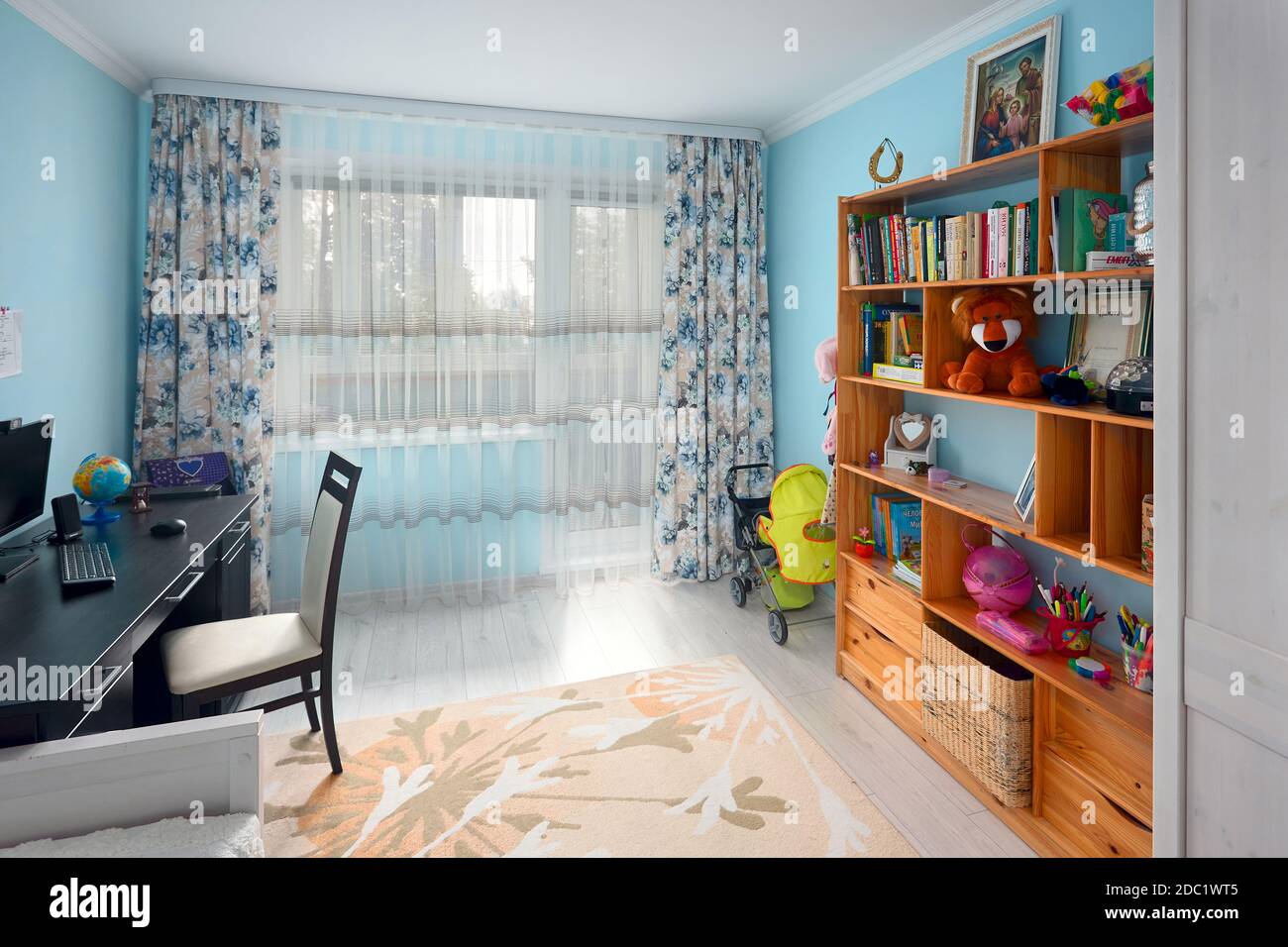 Grodno, Bielorussia, 2020 AGOSTO: Accogliente e luminosa camera per bambini con pareti blu, moquette pastello su pavimento in legno grigio, letto libreria in legno e scrivania con globo Foto Stock