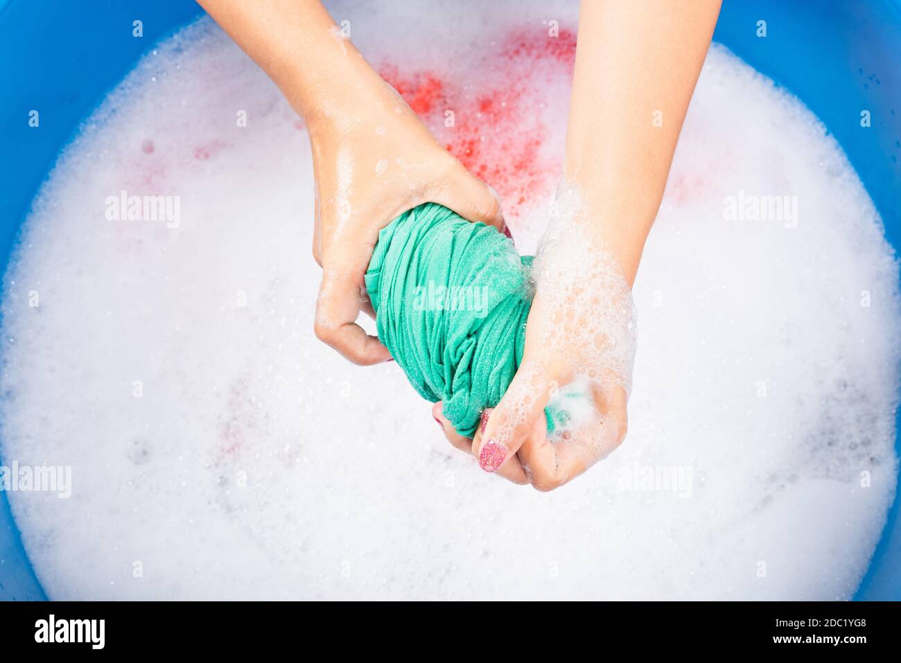 Closeup giovane donna asiatica uso mani lavare abiti colore in bacino. La donna strizzava il panno di tessuto bagnato con detergente e ha bolle di sapone in wate Foto Stock