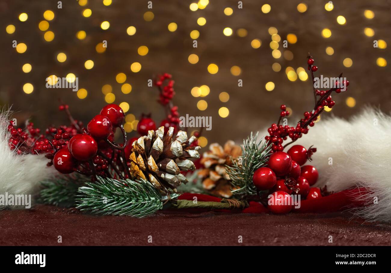 Rami di abete rosso con bacche rosse e coni di pino su un cappello rosso di Babbo Natale con luci di nuovo anno sul retro. Sfondo sfocato. Cartolina di Natale Foto Stock