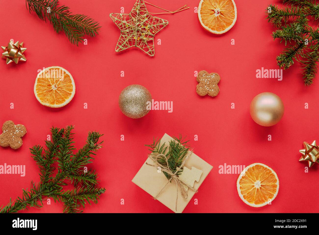 Appartamento di Natale con rami di abete rosso, un regalo, biscotti, arance secche e decorazioni di Natale su sfondo rosso. Concetto di nuovo anno. Vista dall'alto, piatta Foto Stock