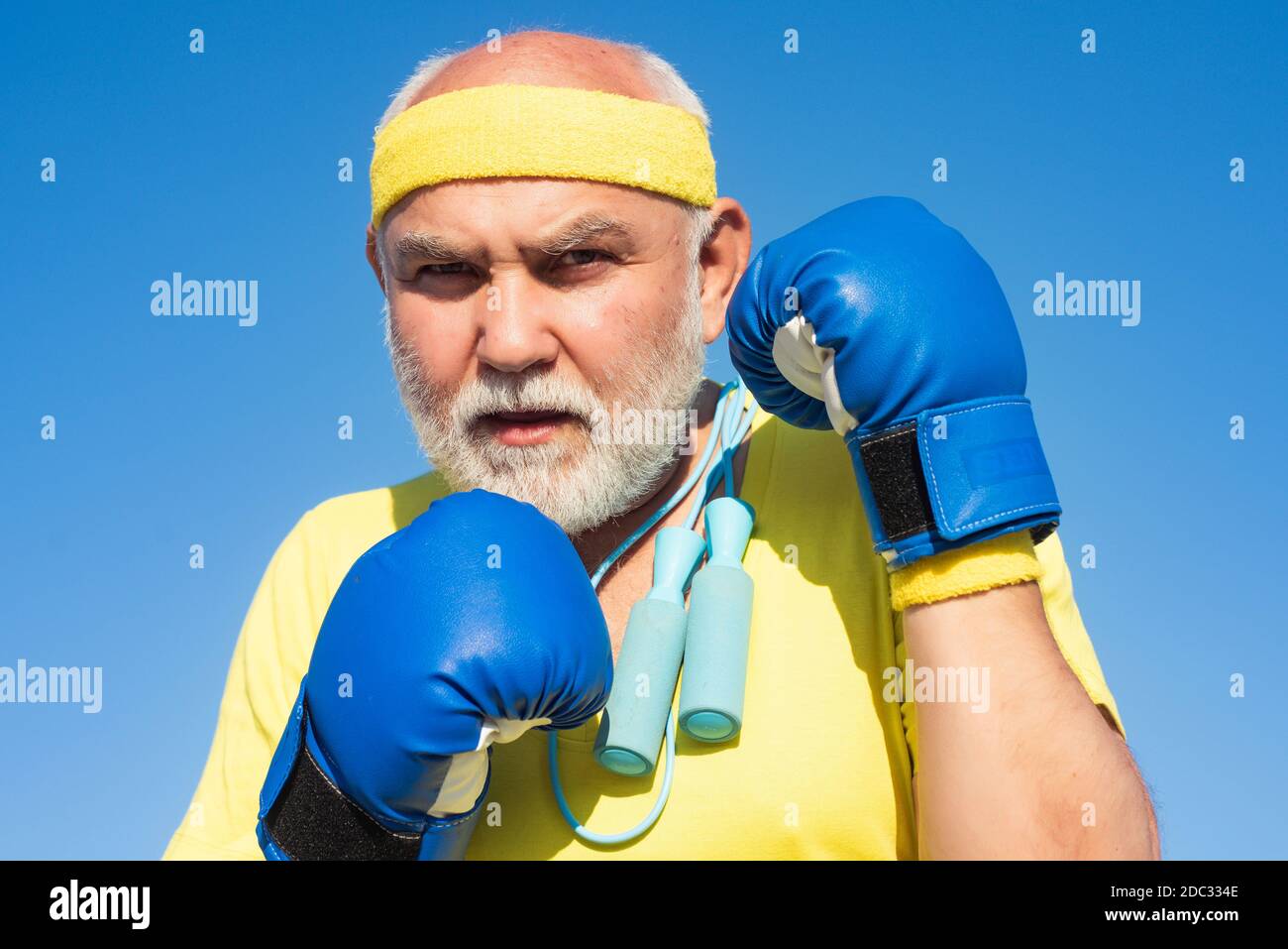 Pugilato uomo anziano - primo piano ritratto. Bell'uomo anziano che pratica i calci di boxe. Uomo sportivo anziano che indossa guanti da boxe. Divertente uomo bearded in piedi Foto Stock