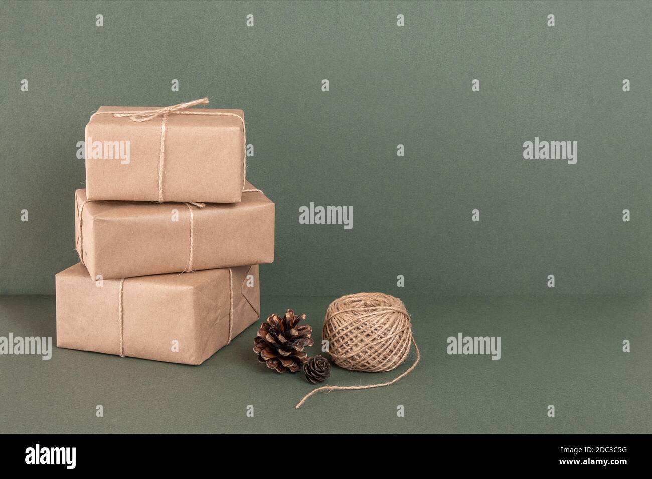 Tre scatole in carta artigianale, spago e coni su sfondo verde. Concept NATALE o Capodanno, Zero Waste Buon Natale. Vista frontale Copia spazio. Foto Stock