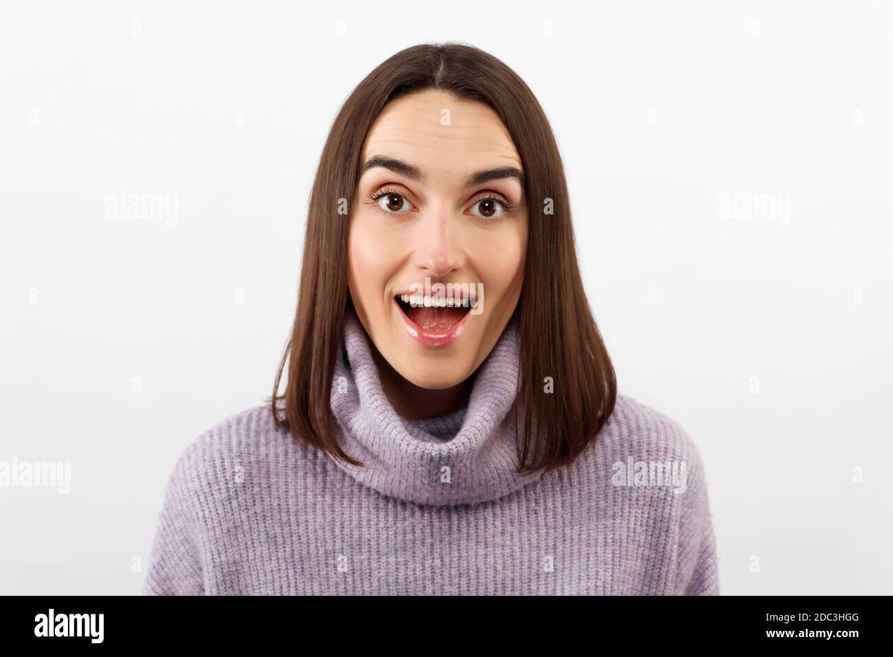 Primo piano seducente donna bruna sorridente in un pullover viola che attende con impazienza un evento emozionante, grinning esprime gioiosamente positività Foto Stock