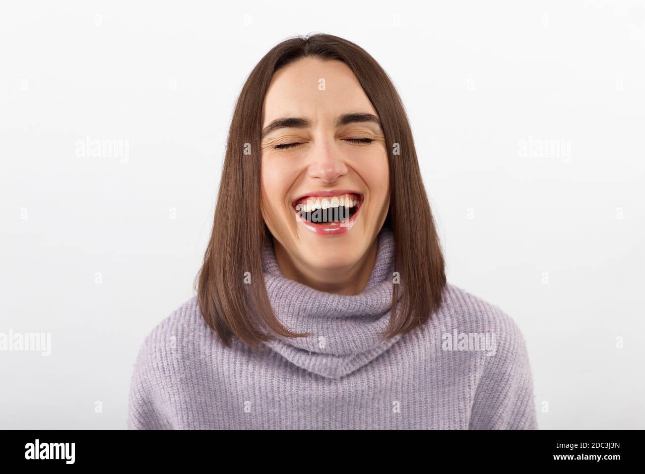 Felice giovane donna allegra che indossa i suoi capelli di brunetto che gioisce a notizie positive o regalo di compleanno, guardando la macchina fotografica con sorriso gioioso e affascinante. Foto Stock