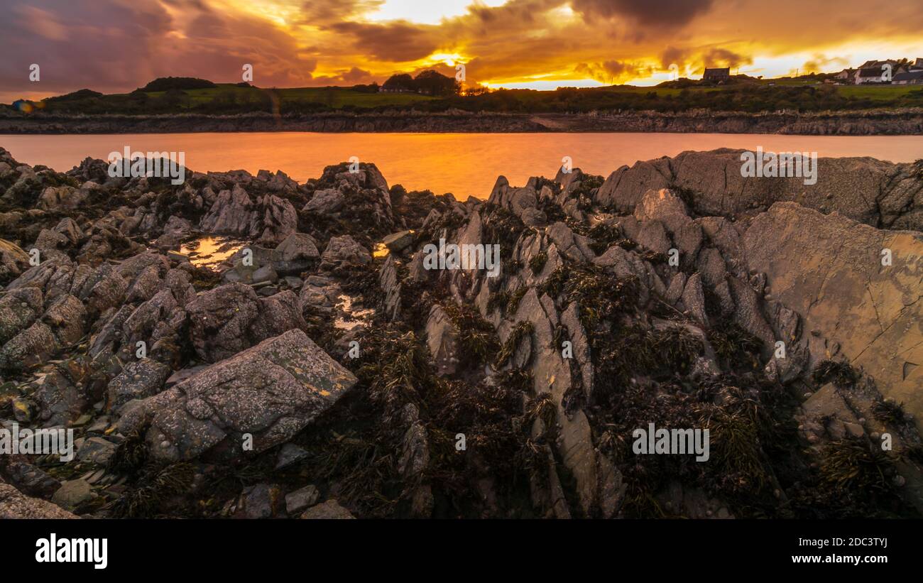 Isola del porto di Whithorn adagiato in un tramonto spettacolare, acqua still e sunburst, spiaggia rocciosa, scogliere Foto Stock