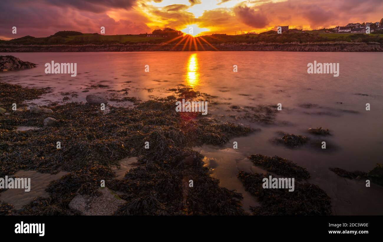 Isola del porto di Whithorn adagiato in un tramonto spettacolare, acqua still e sunburst, spiaggia rocciosa, scogliere Foto Stock