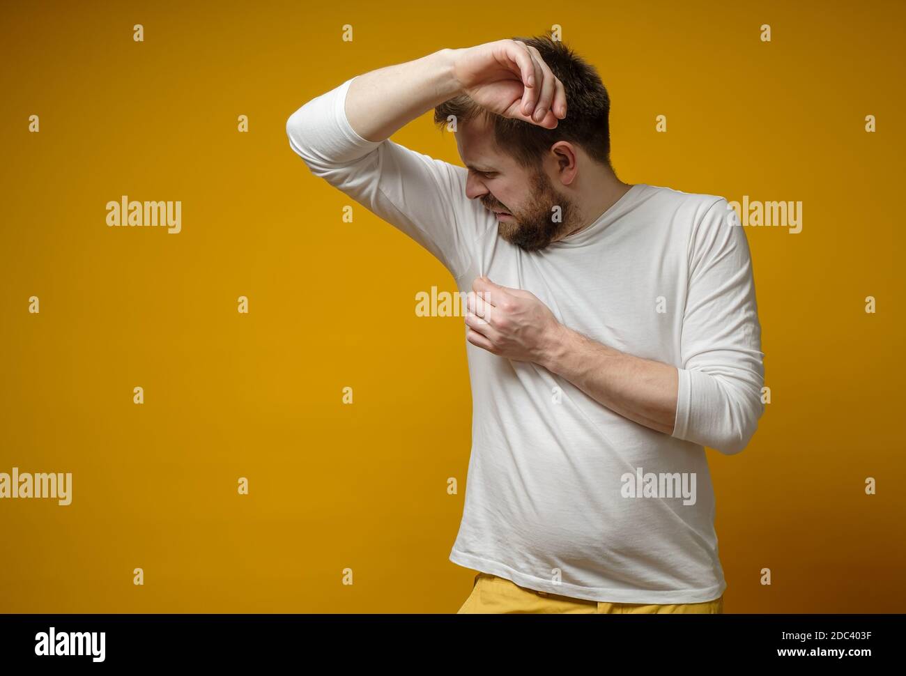 L'uomo in una t-shirt bianca sniffa le sue ascelle, infastidito dal problema della sudorazione e della puzza del corpo. Spazio di copia. Foto Stock