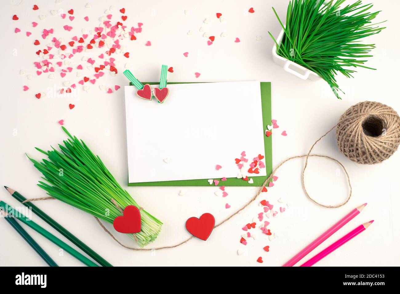 Un bouquet di germogli di grano verde, buste, matite e cuori su uno sfondo chiaro. Foto Stock