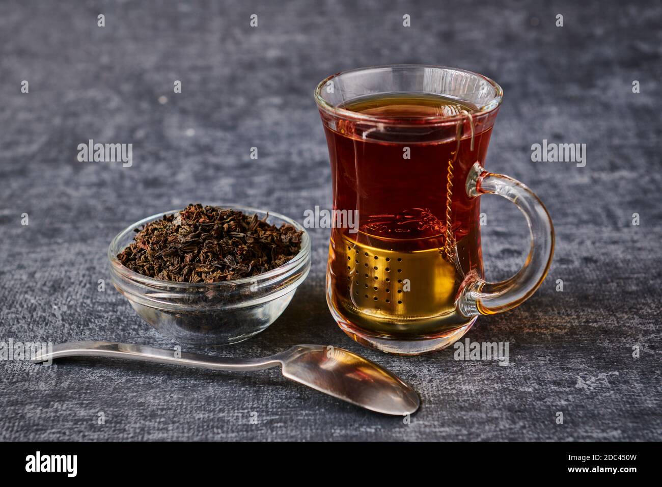 Vista della tazza da tè con setaccio accanto alla presa con preparare e cucchiaino da tè su sfondo grigio Foto Stock