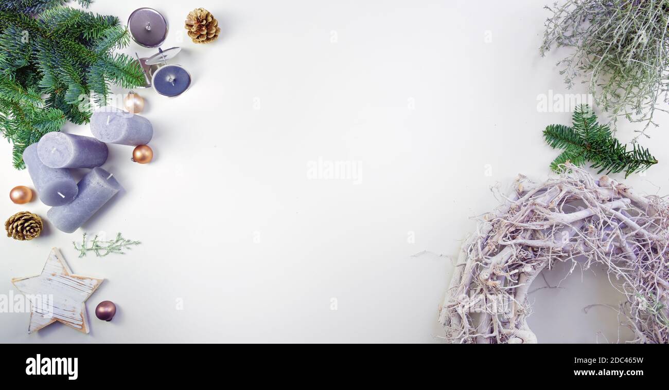 Advent e decorazione di Natale con una corona di legno chiaro, rami di abete, candele di lilla e baubles d'oro opaco su un tavolo bianco, formato panoramico con Foto Stock