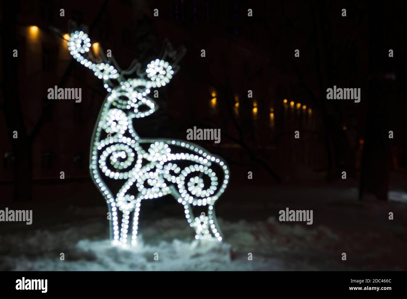 Figura di cervo offuscato da una ghirlanda incandescente nella notte oscura d'inverno nella neve. Sfondo delle vacanze di Natale Foto Stock
