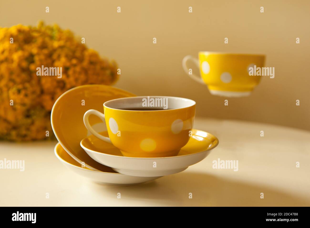 Due tazze da caffè gialle volanti su sfondo bianco, pausa caffè e aggiunta di caffeina concetto. Fiori gialli sul tavolo Foto Stock
