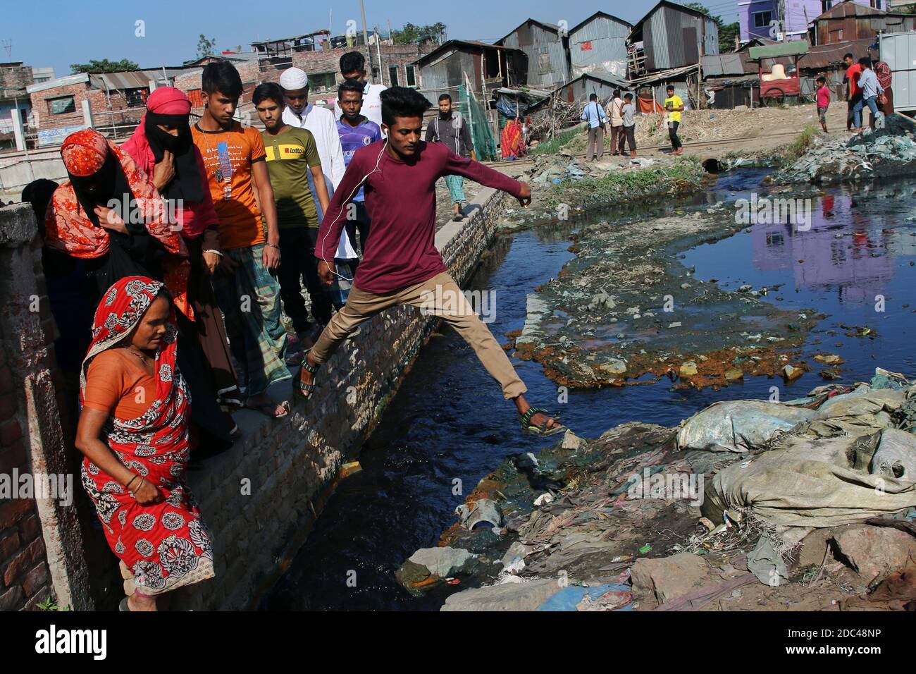 Dhaka, Bangladesh. 12 Nov 2020. La gente è vista attraversare una strada a piedi sopra il muro come la strada è sommersa dagli sprechi dei mulini tessili alla zona industriale di Shyampur in Dhaka.la maggior parte delle persone in questa zona sono diventate vittime di inquinamento a causa della presenza di sostanze chimiche tossiche, principalmente coloranti chimici. A causa di un sistema fognario non pianificato di mulini tessili, i residenti di questa zona soffrono per un lungo periodo di tempo. Credit: SOPA Images Limited/Alamy Live News Foto Stock