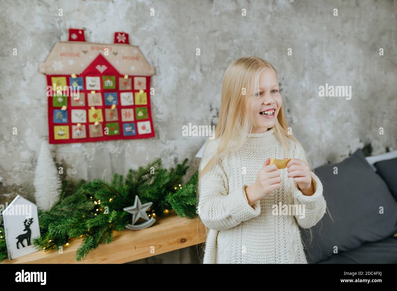 Ragazza che legge un compito dal calendario dell'avvento fatto a mano di Natale in una forma di casa per conto alla rovescia i giorni fino a Natale. Foto Stock