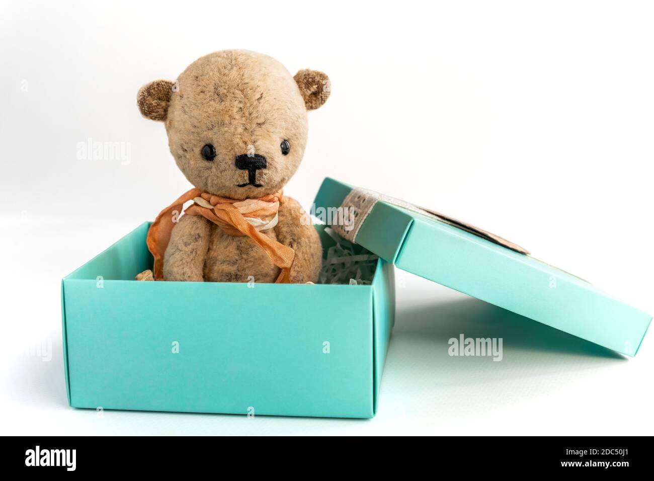 Un piccolo orsacchiotto vintage fatto a mano si trova in una scatola regalo su uno sfondo bianco. Regalo e sorpresa per una vacanza importante. Primo piano. Spazio di copia. Foto Stock
