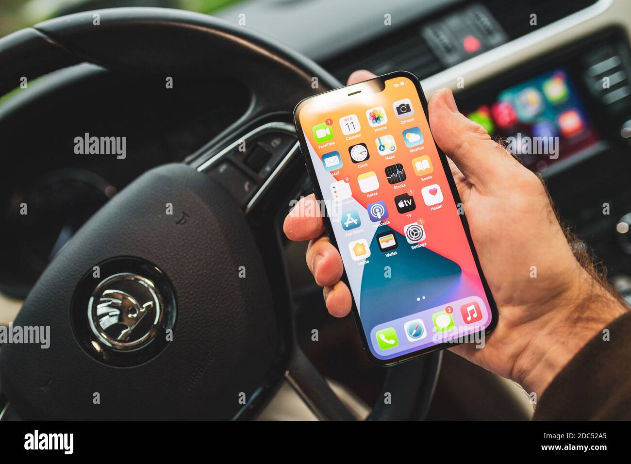 Parigi, Francia - Novembre 11, 2020: Skoda driver holding ultimo iPhone 12 pro con esecuzione in background sistema di computer auto con Apple computer CarPlay da iOS iphone dispositivo - skoda volante Foto Stock
