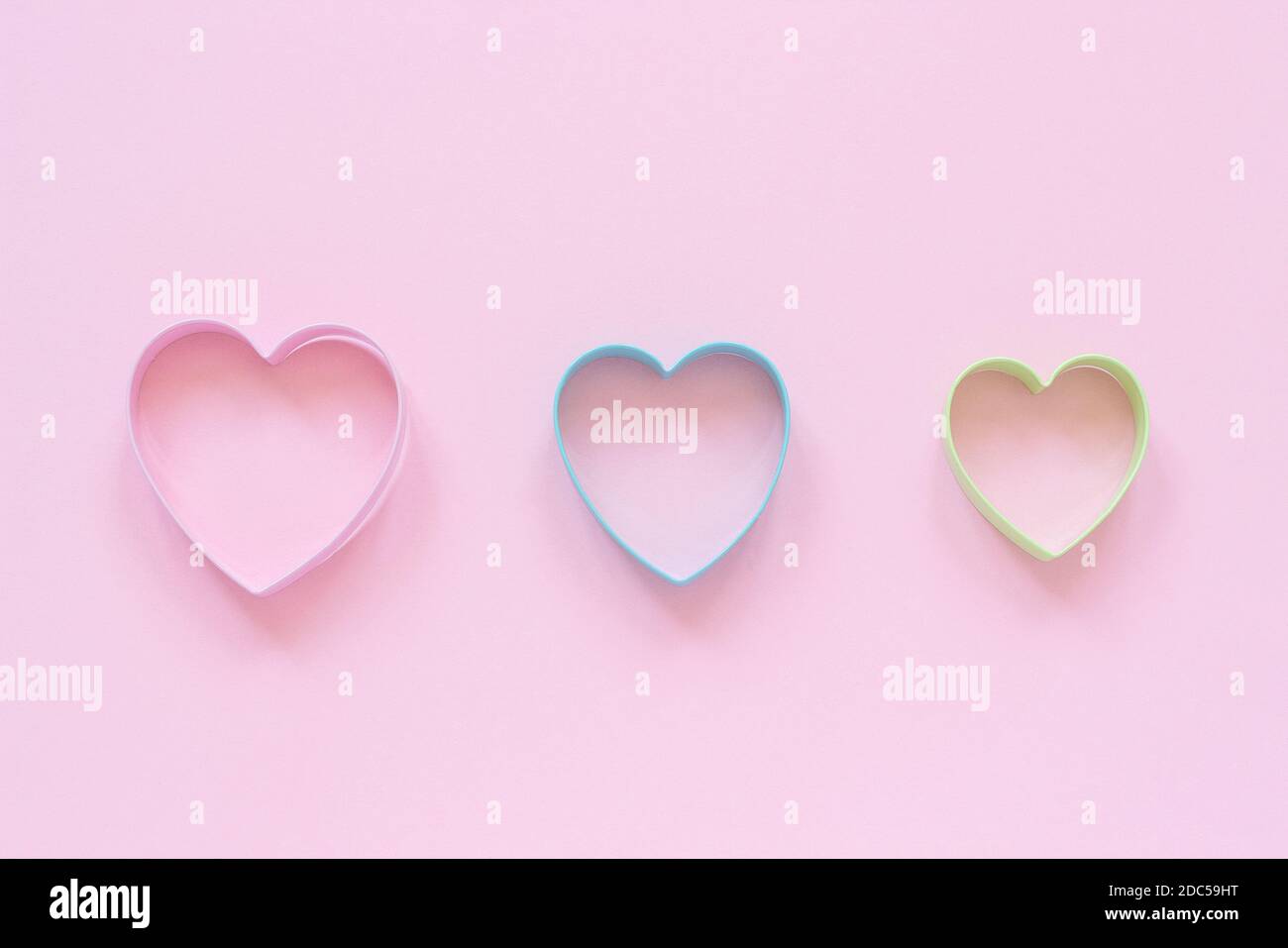 3 biscotti colorati a forma di cuore su sfondo rosa pastello. Carta di San Valentino Concept. Vista dall'alto Copia spazio per il testo. Foto Stock