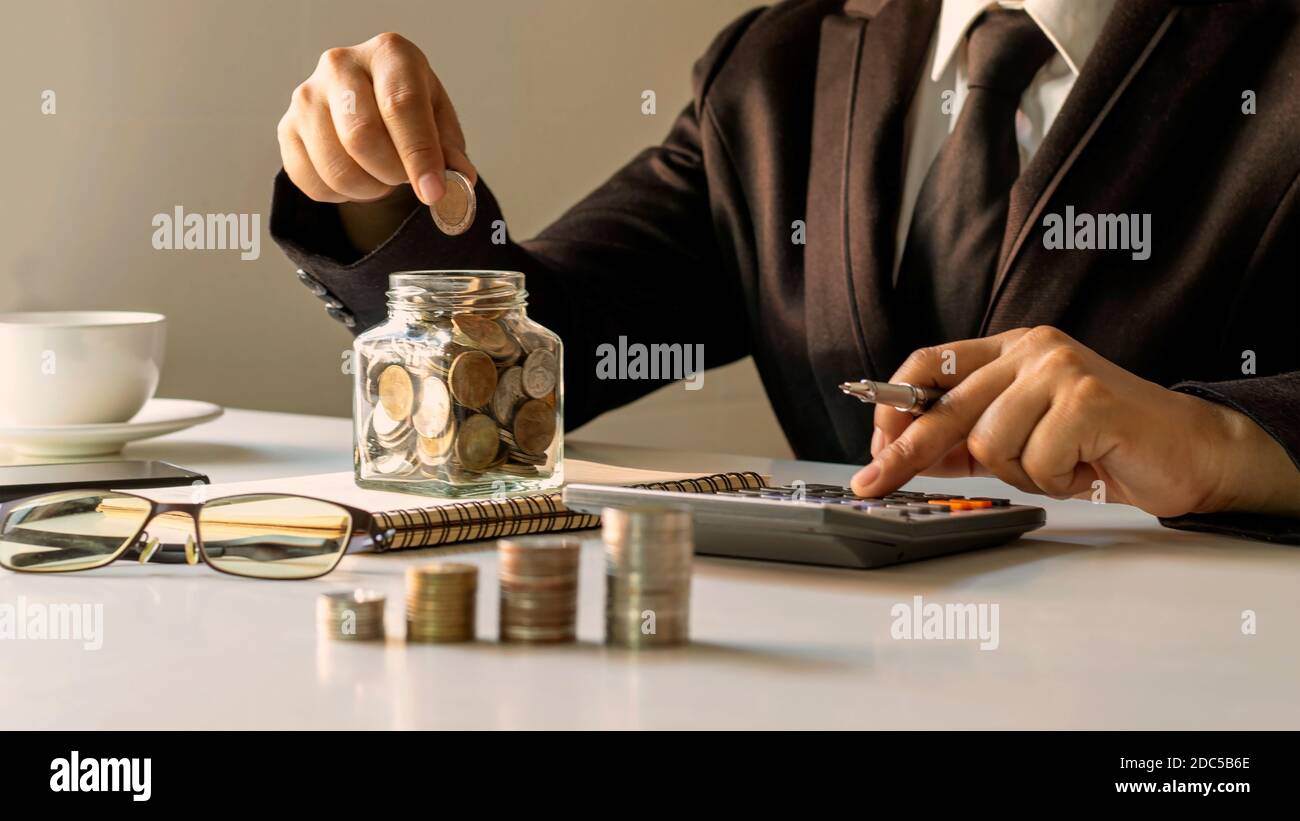 Un uomo d'affari che tiene una moneta in una banca piggy e che preme un concetto finanziario calcolatrice e contabilità finanziaria. Foto Stock