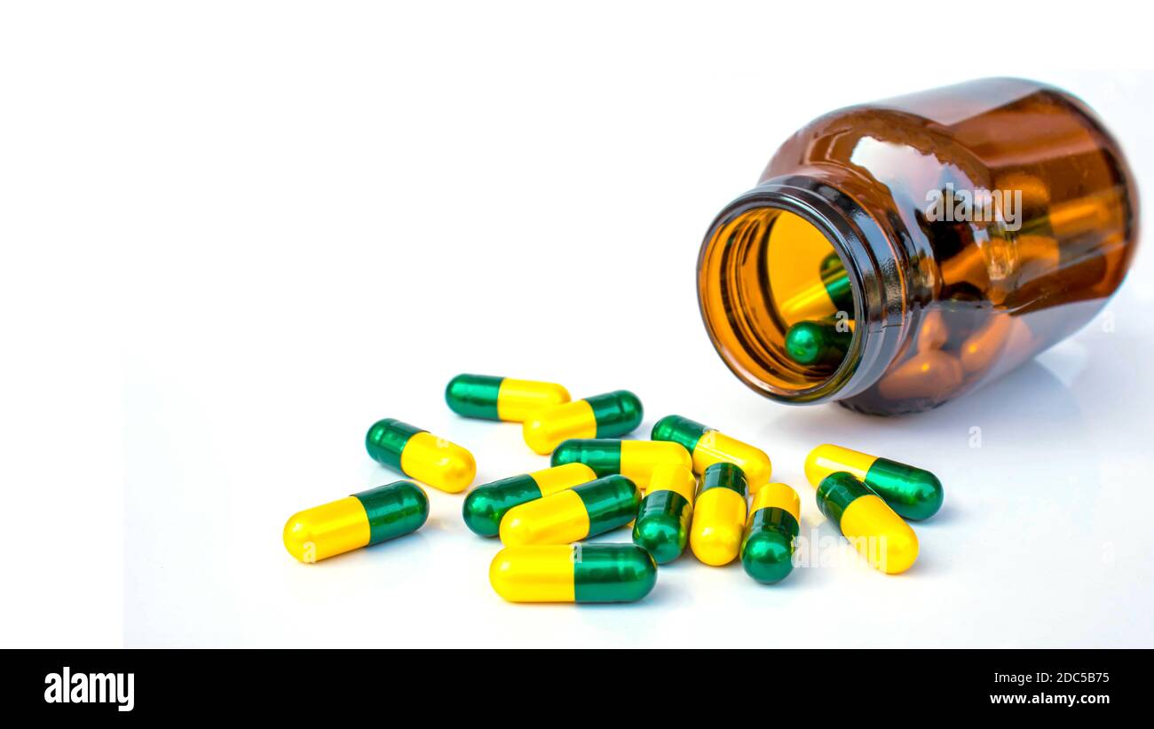 Molte capsule gialle-verdi fuoriescono dal flacone. Isolato su sfondo bianco. Foto Stock