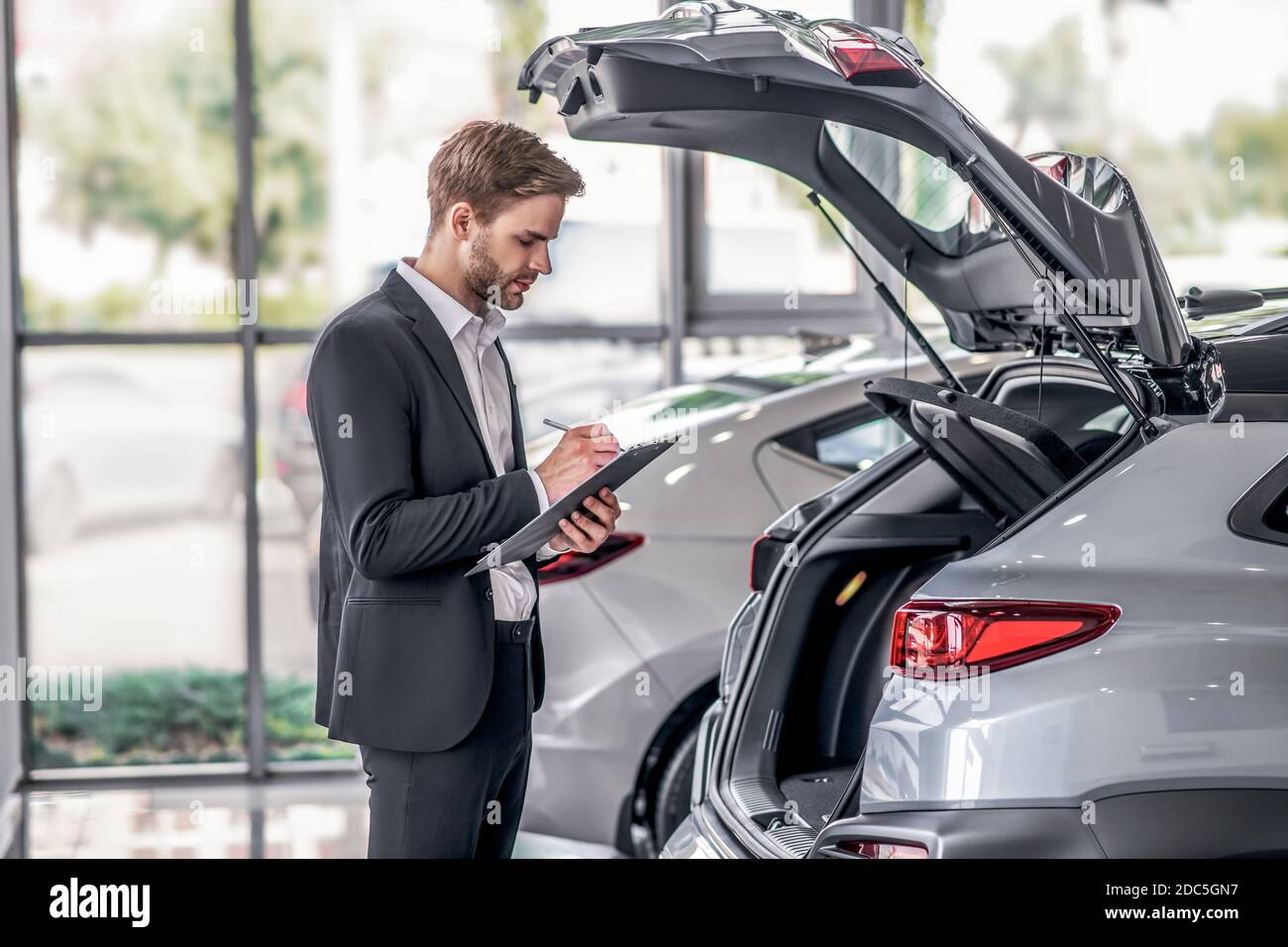 Bearded uomo che esamina scarpone da auto aperto, prendendo appunti nello showroom Foto Stock