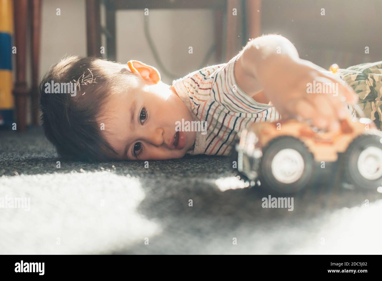 Caucasico ragazzo sta giocando a terra con una macchina sdraiato sulla moquette in giornata di sole Foto Stock