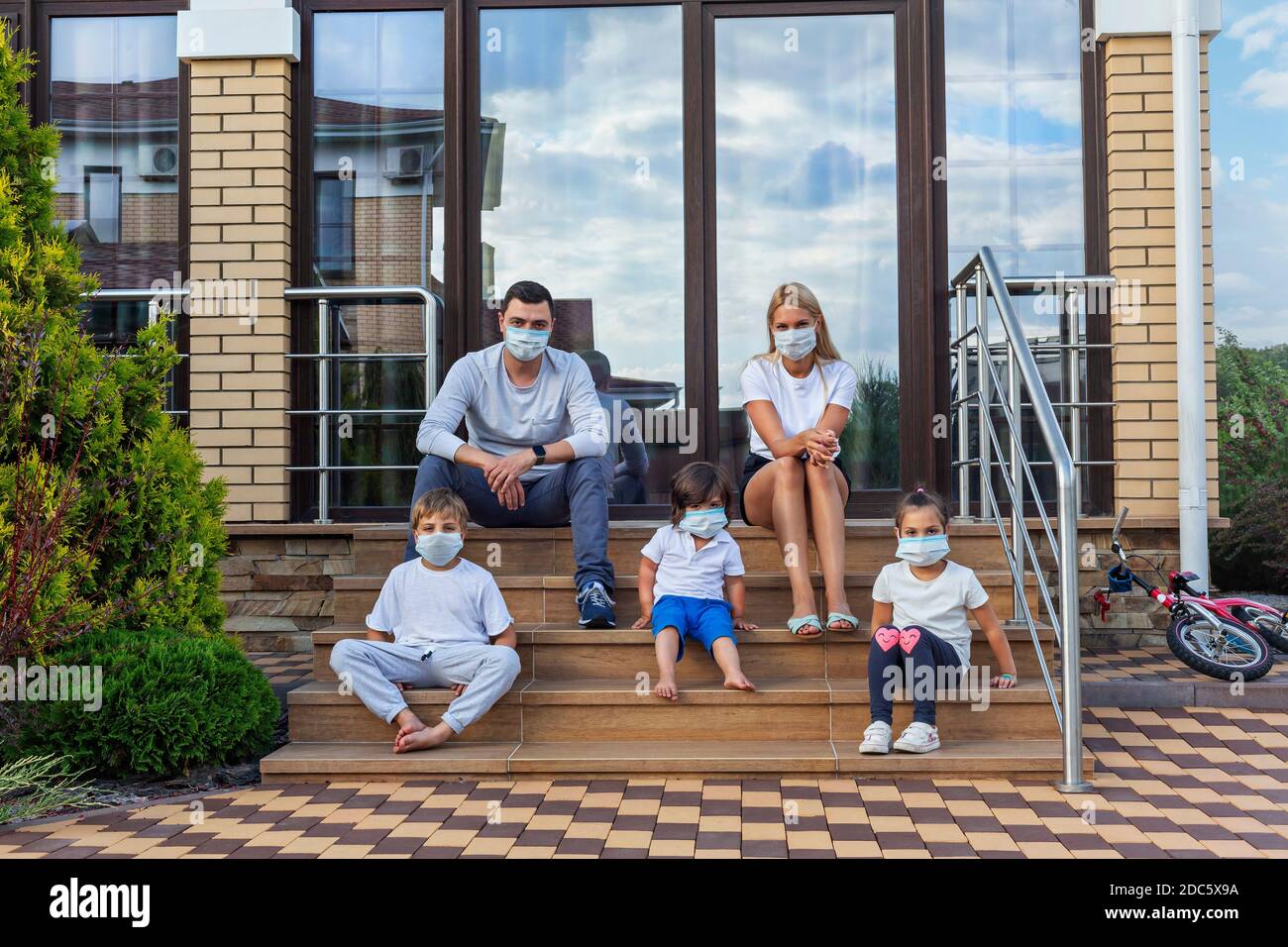 Ritratto famiglia in maschere di faccia su patio gradini di casa Foto Stock
