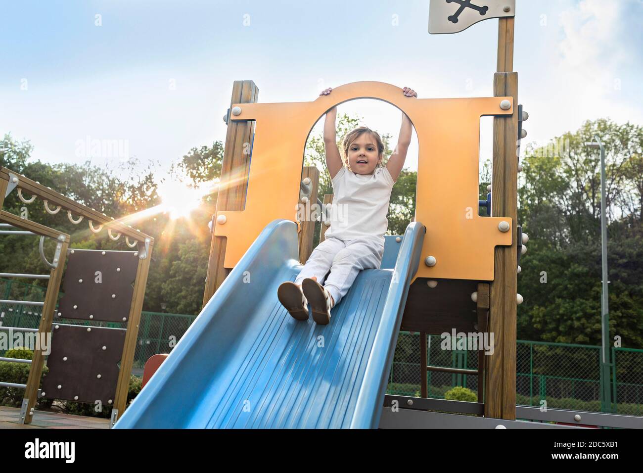 Ritratto ragazza spensierata su scivolo soleggiato parco giochi Foto Stock