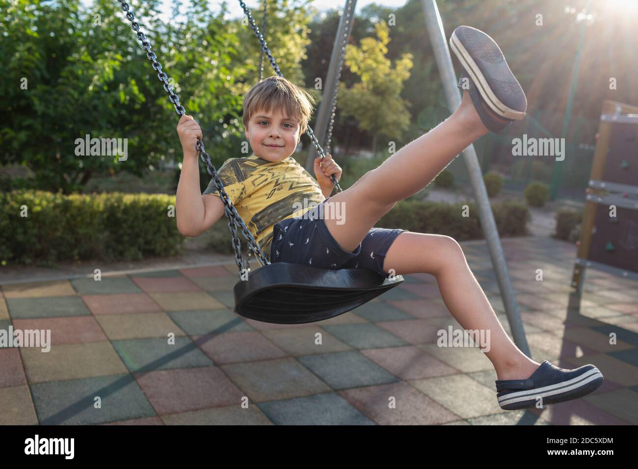 Ritratto ragazzo spensierato che oscilla al parco giochi soleggiato Foto Stock