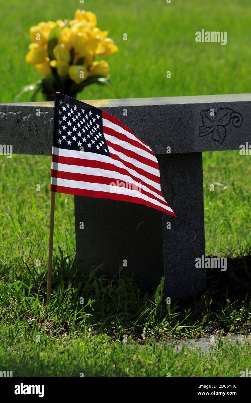 US Flag sparato closeup con fiori gialli e una panchina in Memorial Day che è luminoso e colorato. Foto Stock