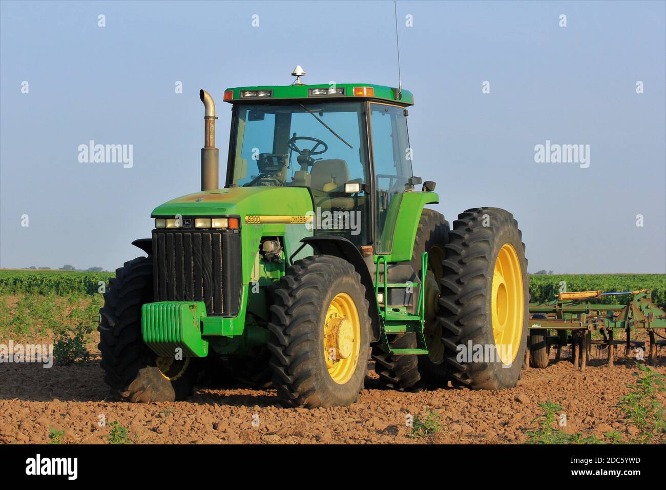 Trattore John Deere in un campo agricolo con un cielo blu e un raccolto verde nel campo. Questo è luminoso e colorato in Kansas. Foto Stock
