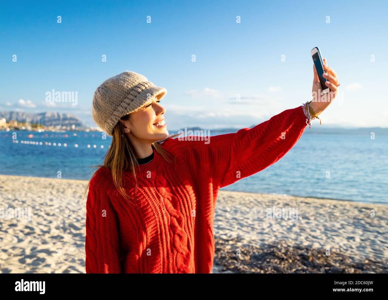 Bella giovane donna caucasica viaggiatore solo fare un ritratto di sé Lei stessa sulla spiaggia al tramonto o all'alba - da sola donna sorridente guardando th Foto Stock
