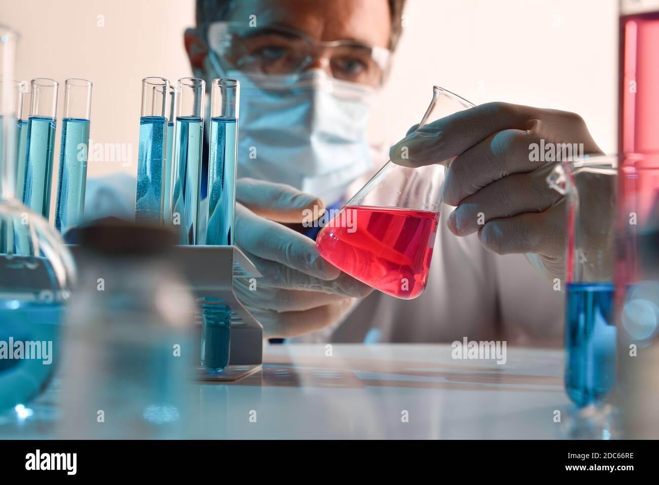 Dettaglio di uno scienziato che manipola con cura un liquido rosso in un pallone su un tavolo da laboratorio. Composizione orizzontale. Vista frontale. Foto Stock