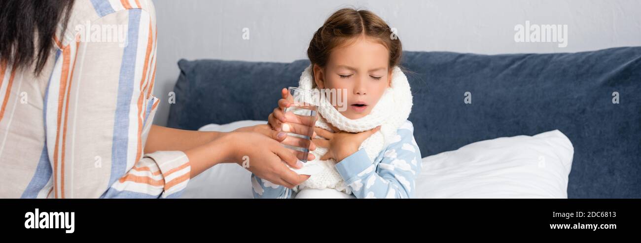 madre che dà un bicchiere d'acqua al bambino malato che tossisce a letto con occhi chiusi, striscione Foto Stock
