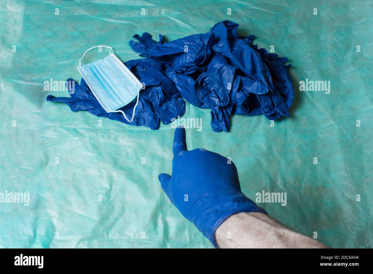Un dito guanto blu punta a un mucchio di attrezzature per la cura personale indossate in ambito sanitario collocato su un tavolo coperto di tessuto chirurgico verde. Foto Stock